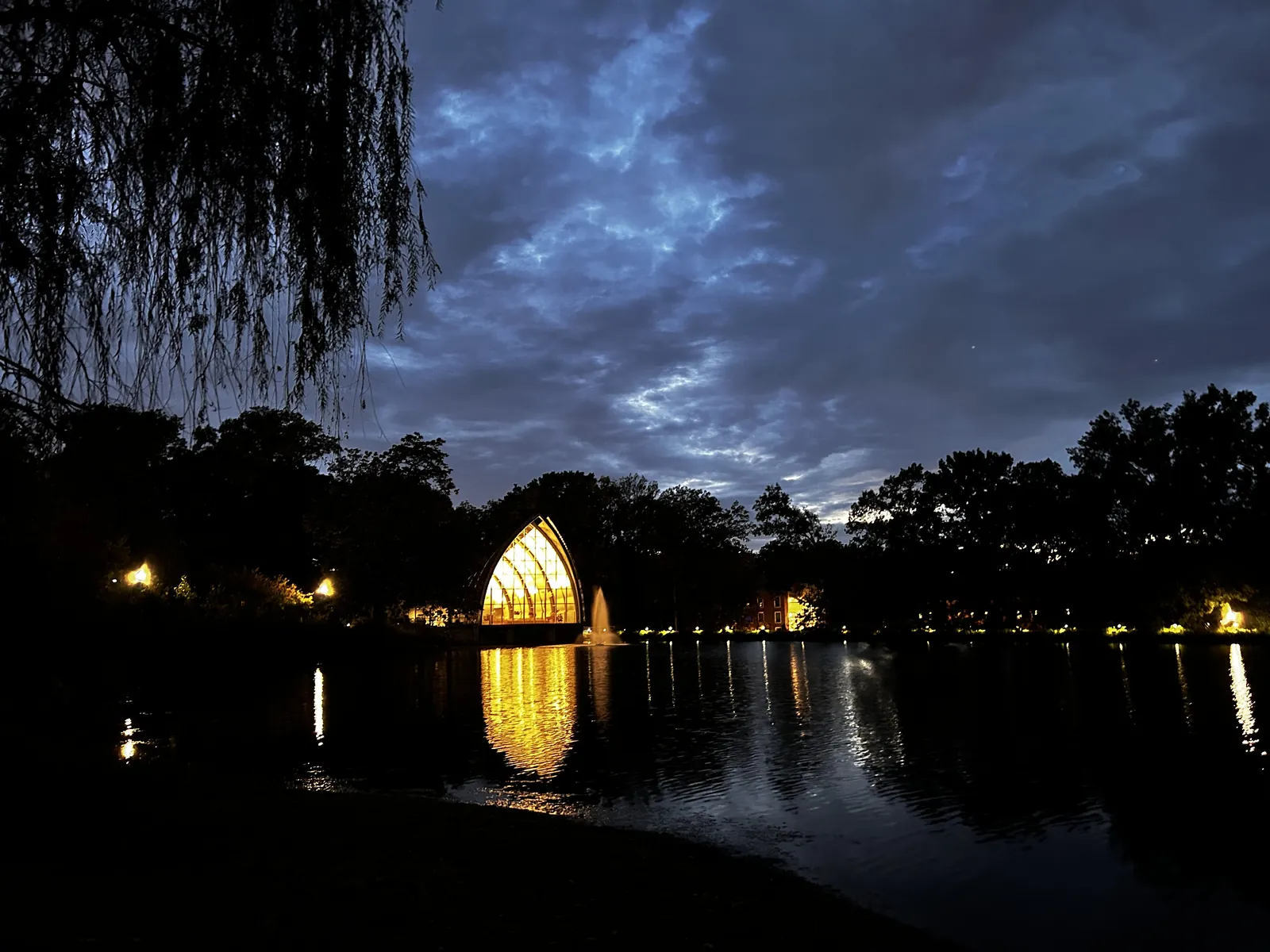 The White Chapel at Rose-Hulman lit gold at dusk, reflected across the lake beneath a deep blue sky.