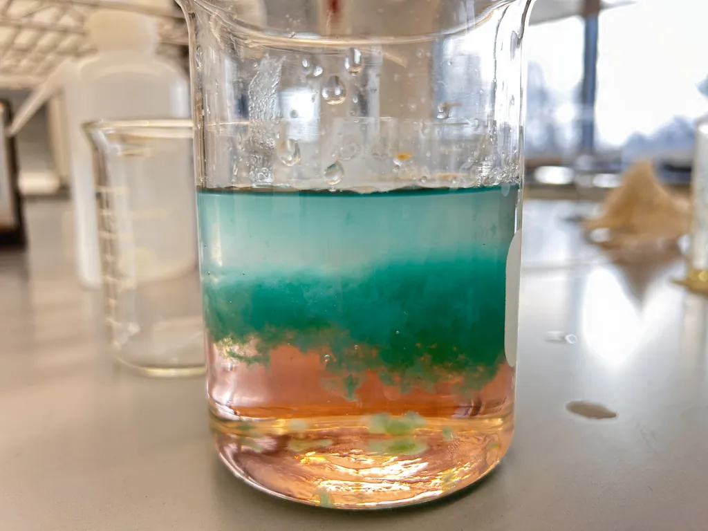 A waste beaker holding two settled layers, teal above and rust orange below.