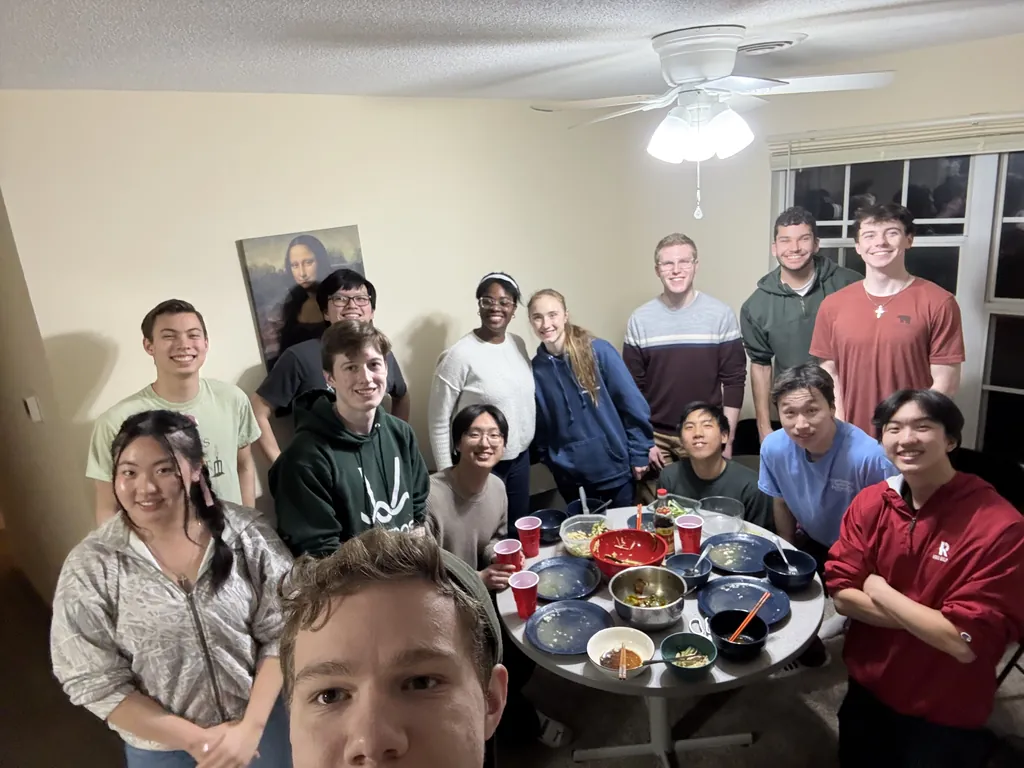 A group crowded around an apartment table full of shared dishes, smiling toward the camera.